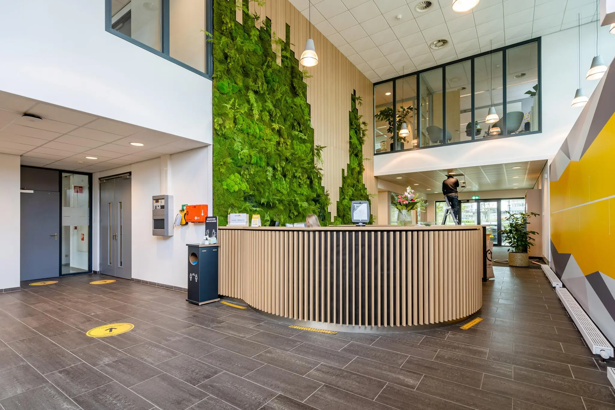 Moderne entreehal aan de Fascinatio Boulevard met groene plantenwand, houten receptiebalie en glazen kantoorruimte op de verdieping.